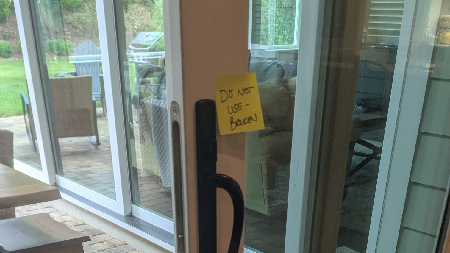 Sliding glass door with a handwritten note taped to the glass reading do not use, broken